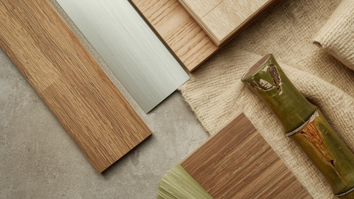 Detalhe editorial de materiais sustentáveis — madeira certificada, alumínio, linho natural e bambu — materiais para arquitetura efêmera dispostos sobre superfície de concreto.
