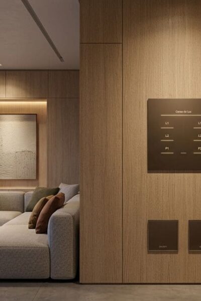 Sala de estar contemporânea com iluminação cênica automatizada e painel de controle minimalista integrado à marcenaria de madeira. Detalhe de interruptores inteligentes embutidos quase invisíveis e design de interiores com tons neutros e luz quente.
